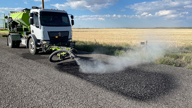 Photo du Cimline P5 en service sur une route rurale. En arrière-plan un champ de maïs et un ciel bleu nuageux.